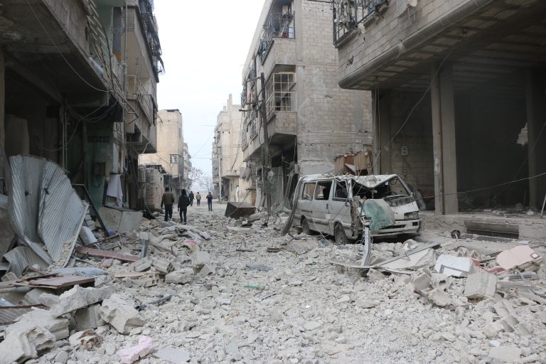 A street covered in rubble with damaged buildings lining either side