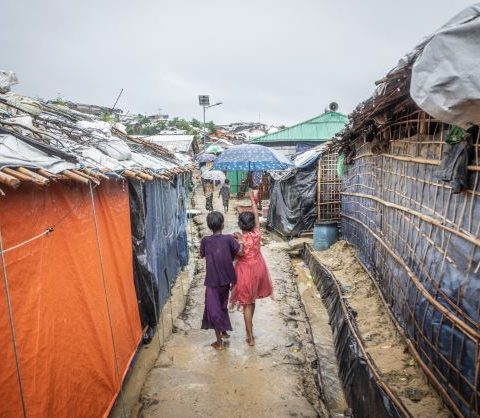 Two girls walk between rows of temporary housing, their backs to the camera
