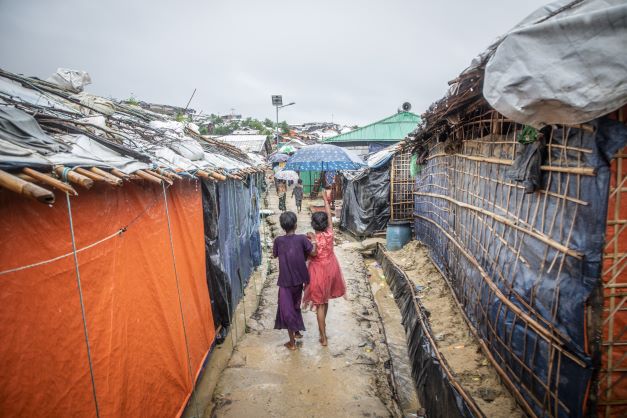 Two girls walk between rows of temporary housing, their backs to the camera
