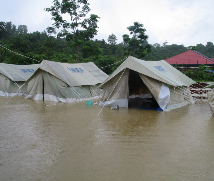 A row of tents with the UNOCHA logo printed ontop are surrounded by brown water.