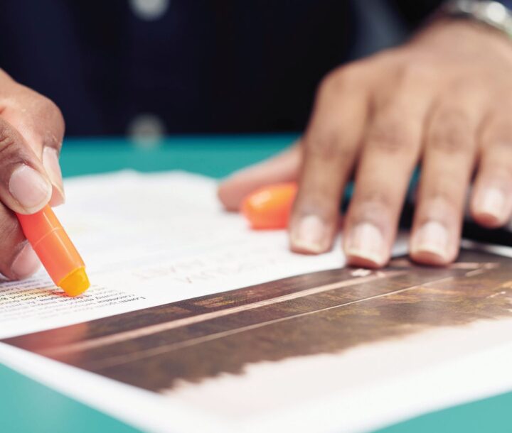 A pair of hands rest of a table. In one hand is an orange marker.