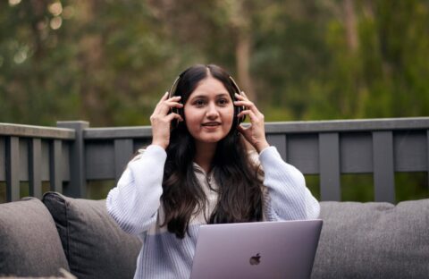 Student sitting outdoors putting on headphones in front of a laptop.