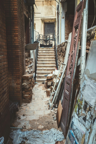 A staircase leads into a door of a decrepit building. In the foreground is debris and a broken door.